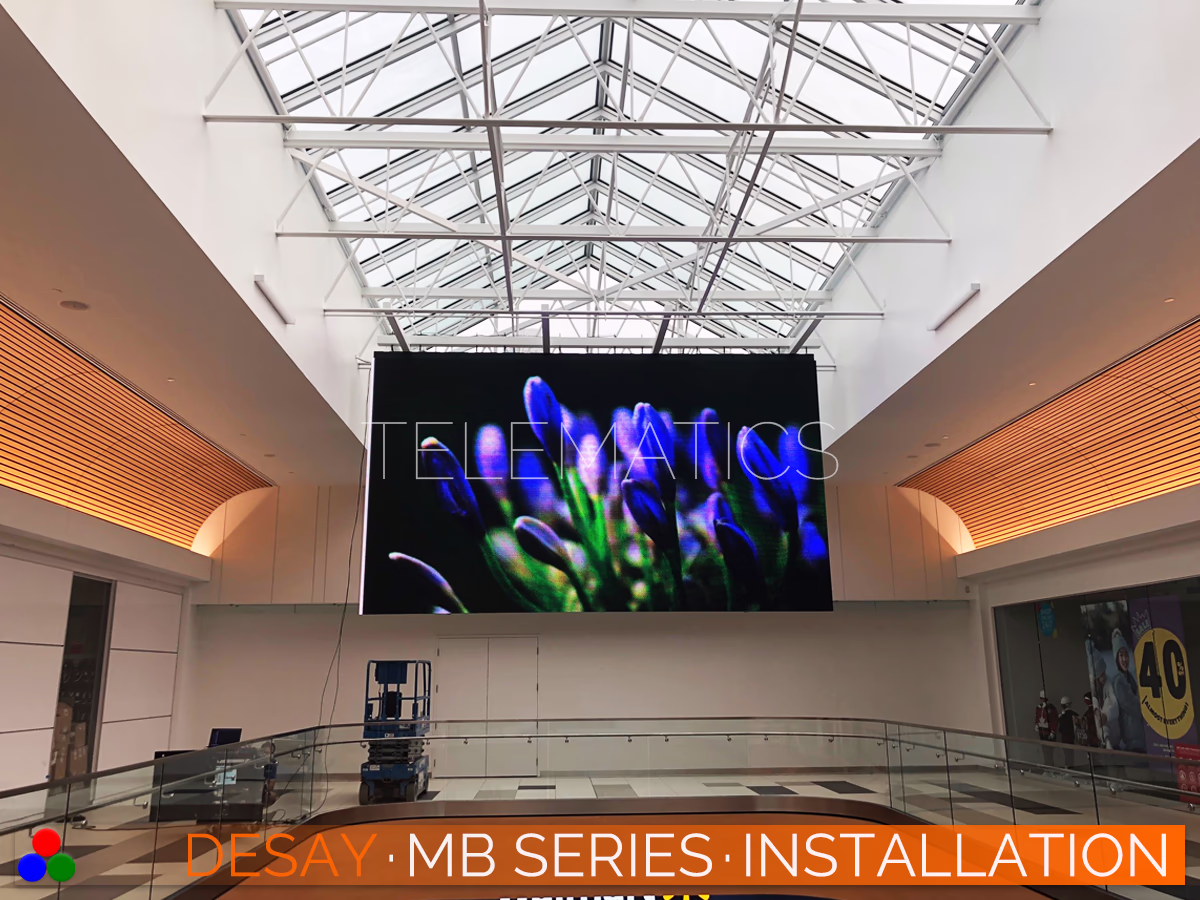 The Art Of LED · Desay MB Series · Telematics Canada Large-scale Desay MB Series LED video wall suspended in a shopping mall atrium, displaying vibrant floral content with high contrast suitable for bright indoor environments.